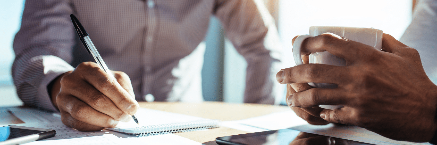 Image of 2 business people at a desk, taking notes and holding a cup of coffee. Illustrates the idea of Fiduciary Disputes in North Carolina Small Business